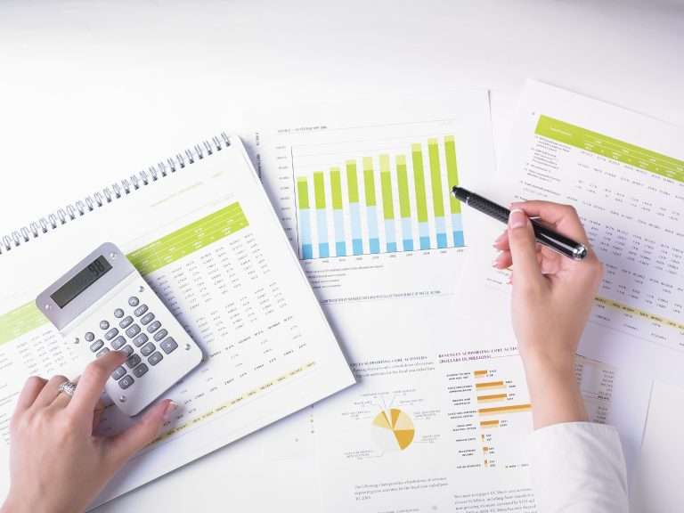 Imagem de uma pessoa analisando gráficos e planilhas financeiras com o auxílio de uma calculadora, representando um processo de avaliação criteriosa de investimentos. A cena remete à busca por decisões financeiras mais conscientes e alinhadas a propósitos, destacando os motivos para investir com impacto: gerar retorno financeiro ao mesmo tempo em que se promove transformação social, proteção ambiental e desenvolvimento sustentável.