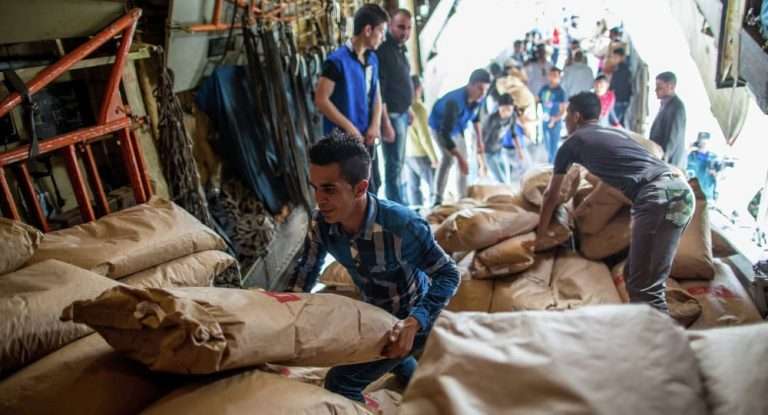 Imagem mostra pessoas descarregando sacos de alimentos de um avião cargueiro, em uma clara ação humanitária. A cena retrata o trabalho intenso de uma operação de ajuda coordenada, com foco no apoio a comunidades vulneráveis. Esta imagem simboliza a atuação do terceiro setor, que promove respostas rápidas a crises e contribui diretamente para o bem-estar social e o fortalecimento da economia local por meio da mobilização de recursos, geração de empregos e prestação de serviços essenciais.