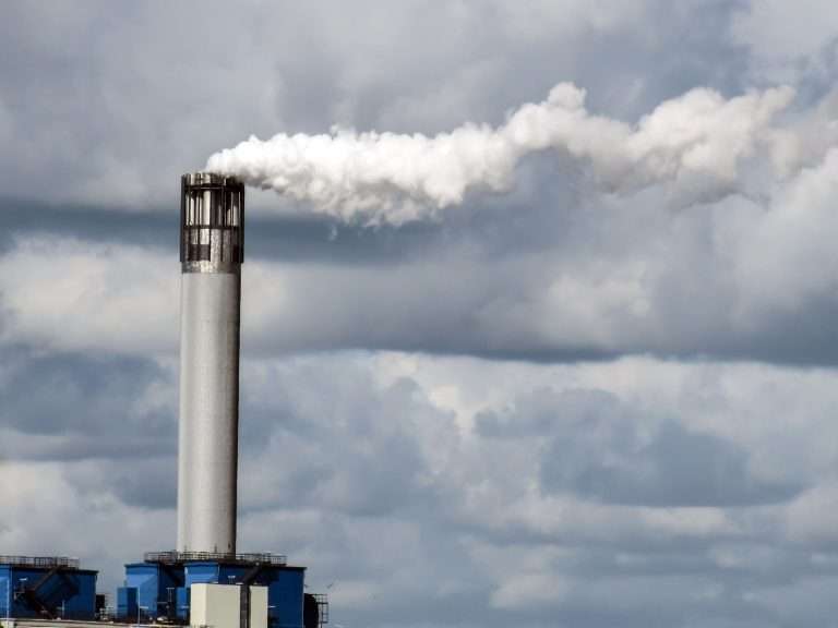 Chaminé industrial emitindo fumaça branca sob um céu nublado, representando emissões de carbono e os desafios enfrentados pelo financiamento climático para apoiar uma transição justa e sustentável.