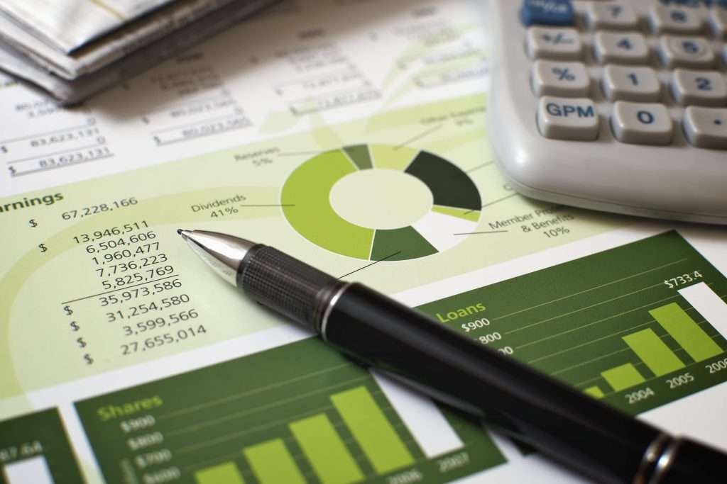 Gráfico financeiro com paleta de cores verdes, planilhas com dados de receita, lucros e dividendos, caneta e calculadora sobre a mesa, sugerindo análise de investimentos com foco em sustentabilidade.