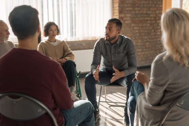 Grupo de pessoas sentadas em roda durante encontro ou sessão de apoio.