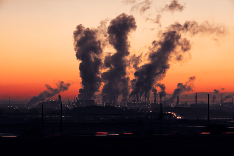 Complexo industrial emite fumaça na atmosfera durante o pôr do sol, ilustrando os desafios das emissões de gases de efeito estufa e a importância da mitigação climática para reduzir os impactos das mudanças climáticas.